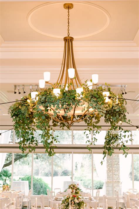 A Chandelier Hanging From The Ceiling With Greenery And Candles On It