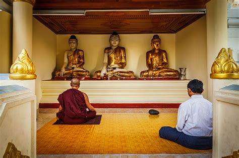 Man And Buddhist Monk Meditating And Worshipping Statues Of Buddha In