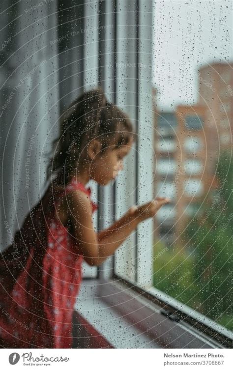 Little Girl Looking Through The Window In Her Bedroom In A Rainy Day