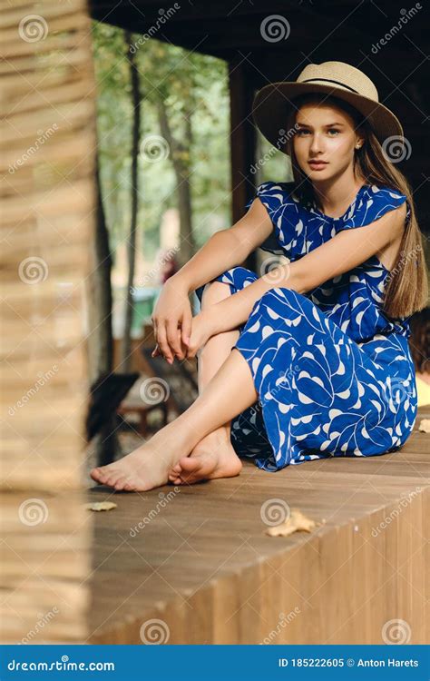 Young Beautiful Woman In Blue Dress And Hat Barefoot Thoughtfully