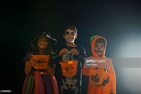 Portrait Of Brothers And Sister Wearing Halloween Costumes Holding