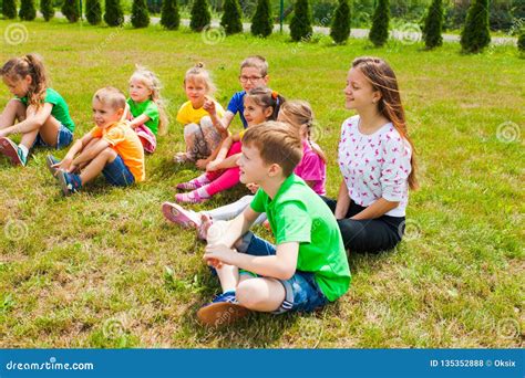 Smiling Children Sitting On A Grass At Outdoor Lesson Stock Photo