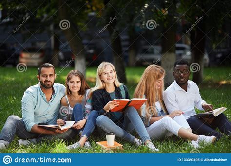 Mixed Race Group Of Students Sitting Together On Green Lawn Of