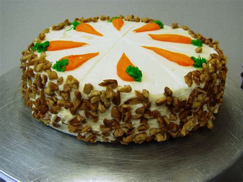A Carrot Cake With White Frosting And Green Leaves On Top Is Sitting On A Silver Platter