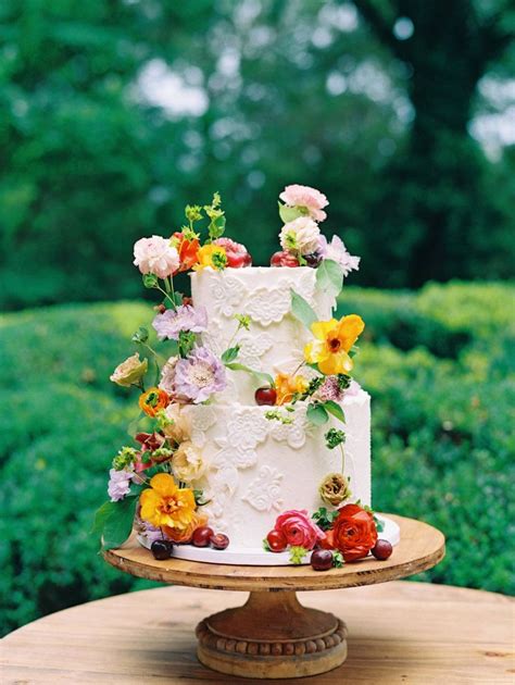 a white wedding cake with flowers on top sitting on a wooden table in front of bushes