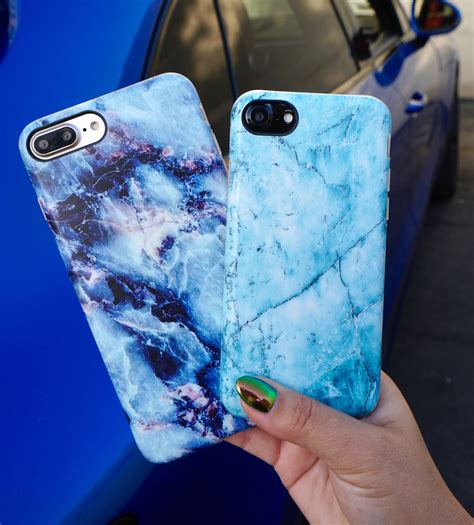 Two Blue Marble Iphone Cases Being Held By A Womans Hand In Front Of A Car