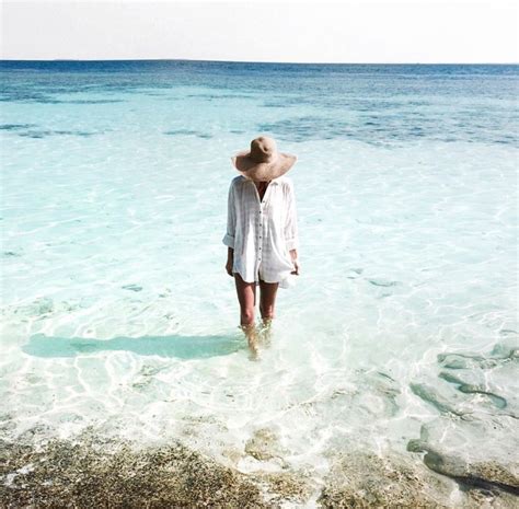 A Woman Standing In Shallow Water With Her Hat On Looking At The Ocean