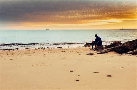 Hombre caucásico solo sentado en la orilla del mar Foto Premium