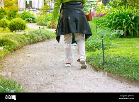 A Woman Strolling Alone Along A Winding Dirt Path In A City Park Amidst