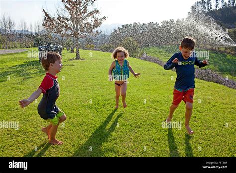 Tres Enérgicos Niños Corriendo A Través De Un Rociador Sobre El Césped