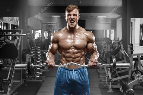 Hombre musculoso ejercitándose en el gimnasio haciendo ejercicios con barra en bíceps fuertes