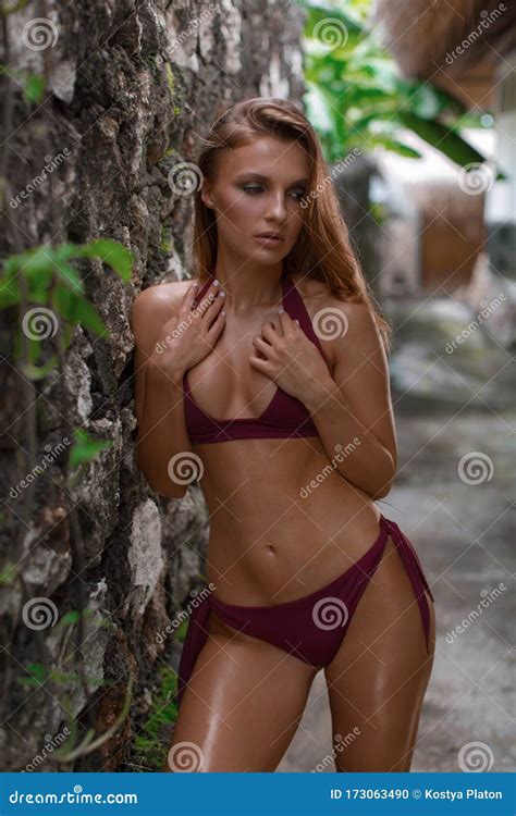 Stunning Tanned Brunette Posing In Burgundy Bikini Standing Near Stone