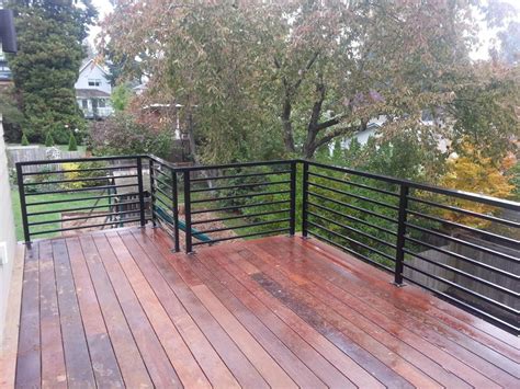 This wood privacy handrail uses 1×2 slats running horizontally between top and bottom 2×4 rails with a square metal pipe railings with vertical balusters below triple horizontal top rails are attached to the face of a stone balcony which curves away in an arc. Aluminum Railings | American Railworks