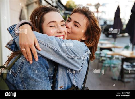close up photo of two emotional happy woman friends hugging each other on city street stock