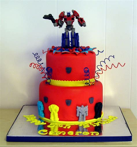 a red and yellow birthday cake with robot figures on the top surrounded by confetti streamers
