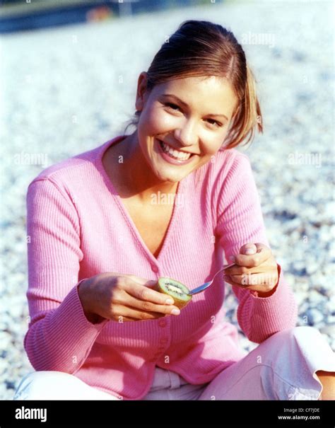 Female Fair Hair Off Her Face Wearing A Pink Cardigan And White Cropped Trousers Sitting On