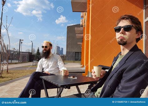 Two Young Hipster Guy Sitting In A Cafe Chatting And Drinking Coffee