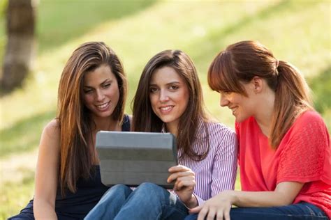 Three Woman Sitting On Grass And Looking At A Digital Tablet Stock