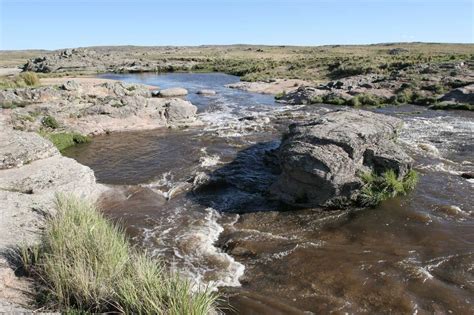 A River Running Through A Rocky Landscape With Grass In The Foreground And Rocks In The Background