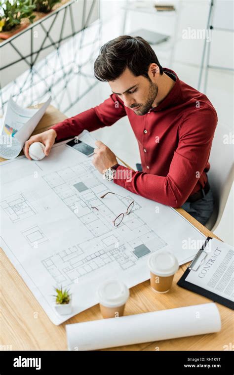 Handsome Male Architect Sitting And Working On Blueprint In Office