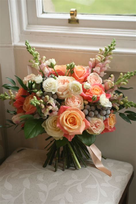 Asymmetrically draped tulle overlays the strapless. Wedding bouquet in pink and peach with roses, snapdragons ...