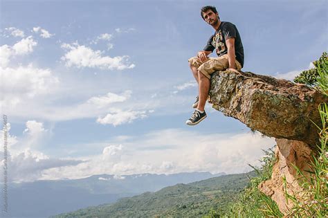 Man Sitting On A Rock With His Feet Dangling Off The Edge On Nature