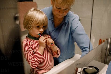 Grandmother With Grandson Brushing Teeth In Bathroom At Home Stock Photo