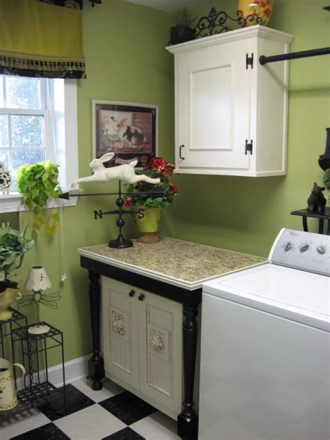 This well appointed green laundry room is lit by a glass and brass bell jar lantern hung over green cabinets topped with a white quartz countertop holding a sink with a chrome faucet beneath a window. A Happy Green Laundry Room - Southern Hospitality
