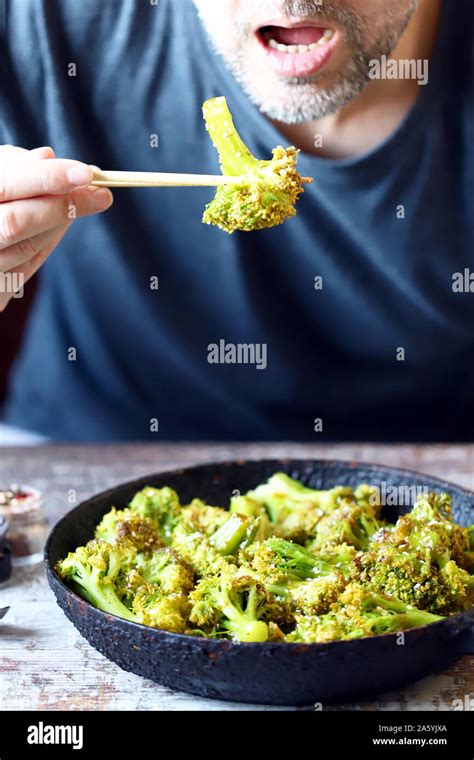A Man Puts Broccoli In His Mouth With Chopsticks Cooking Broccoli