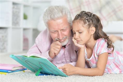 Grandfather Reading Book With His Little Granddaughter Stock Photo