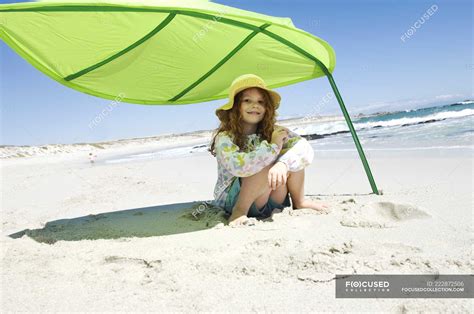 kleines mädchen sitzt auf einem grünen zelt am strand und blickt in die kamera — kind
