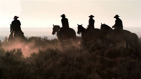 Slow Motion Shot Of Cowboys Riding Through Sagebrush In The Desert In