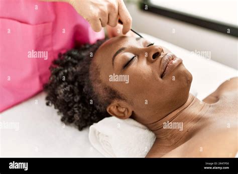 African American Woman Lying On Massage Table Having Eyebrows Treatment At Beauty Salon Stock