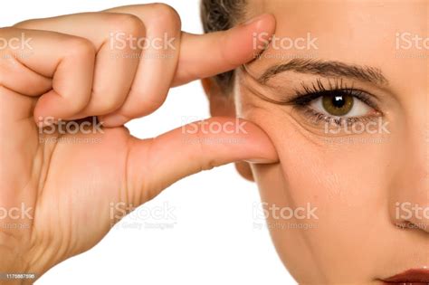 Young Woman Pinching Her Eye Wrinkles With Her Fingers On A White