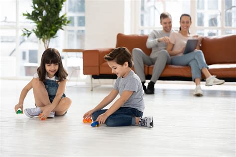 Parents Relaxing Using Device On Sofa Kids Play On Floor Stock Photo