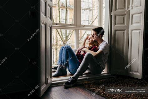 Young Couple Sitting On Window Sill And Hugging — Joyful Togetherness