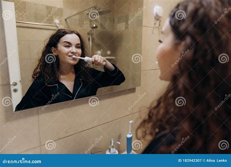 Portrait Of A Beautiful Woman Brushing Teeth And Looking In The Mirror