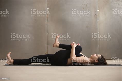 Young Woman In Knees To Chest Apanasana Pose Grey Studio Stock Photo