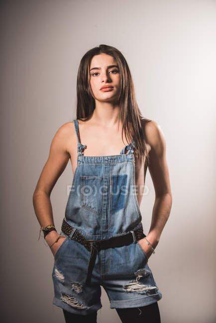Front View Of Brunette Topless Girl Posing In Denim Overall And Looking