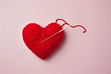 Red Wool And A Knitting Needle Are On Top Of The Red Heart Background
