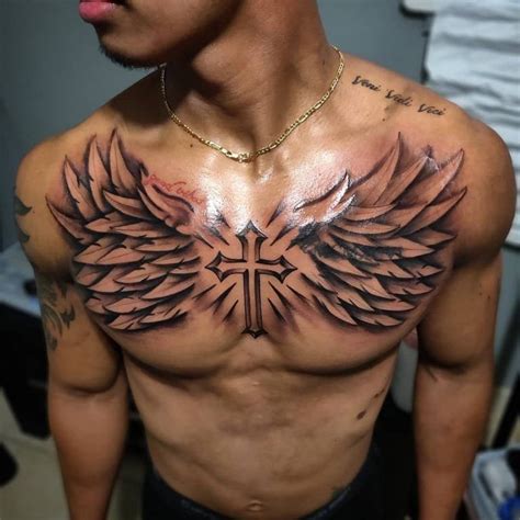 A Man With Tattoos On His Chest Has An Angel Cross And Wings Tattoo On