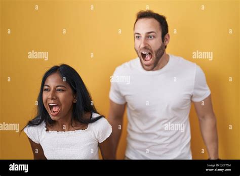 Interracial Couple Standing Over Yellow Background Angry And Mad