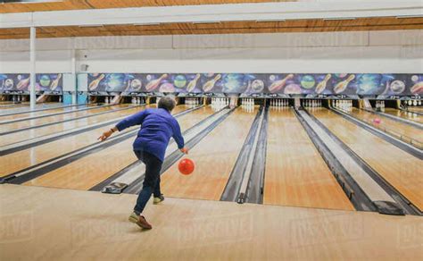 Older Woman Throwing Bowling Ball Down A Bowling Lane Stock Photo