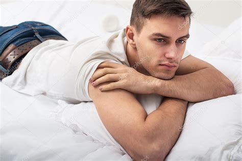 Handsome Man Guy In White T Shirt And Blue Jeans Lying On A Bed Stock