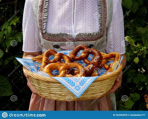 Woman In Traditional Bavarian Dirndl Dress Holding A Basket Of Pretzels