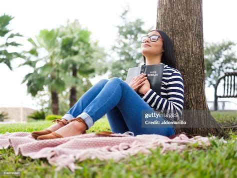 Pretty Young Woman Sitting Next To Tree And Holding Bible High Res