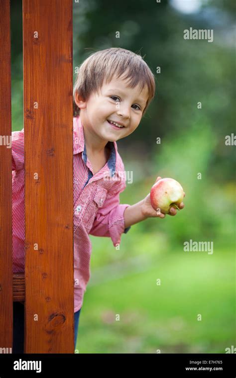 Adorable Boy Holding Apple Standing Next To Wooden Door Stock Photo
