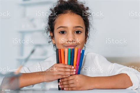 Adorable African American Kid Holding Colored Felt Pens And Looking At