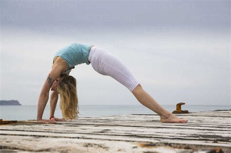 Mid Adult Woman Bending Over Backwards Practicing Yoga On Wooden Sea
