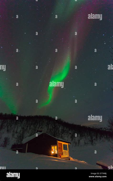 Northern Light Aurora Borealis With A Cottage Cabin With Lights From